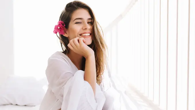 033211400_1756191125-romantic-girl-with-sly-smile-vintage-blouse-sitting-bed-touching-her-chin-with-hand-portrait-dreamy-cute-young-woman-with-flower-hairstyle-resting-bedroom-morning